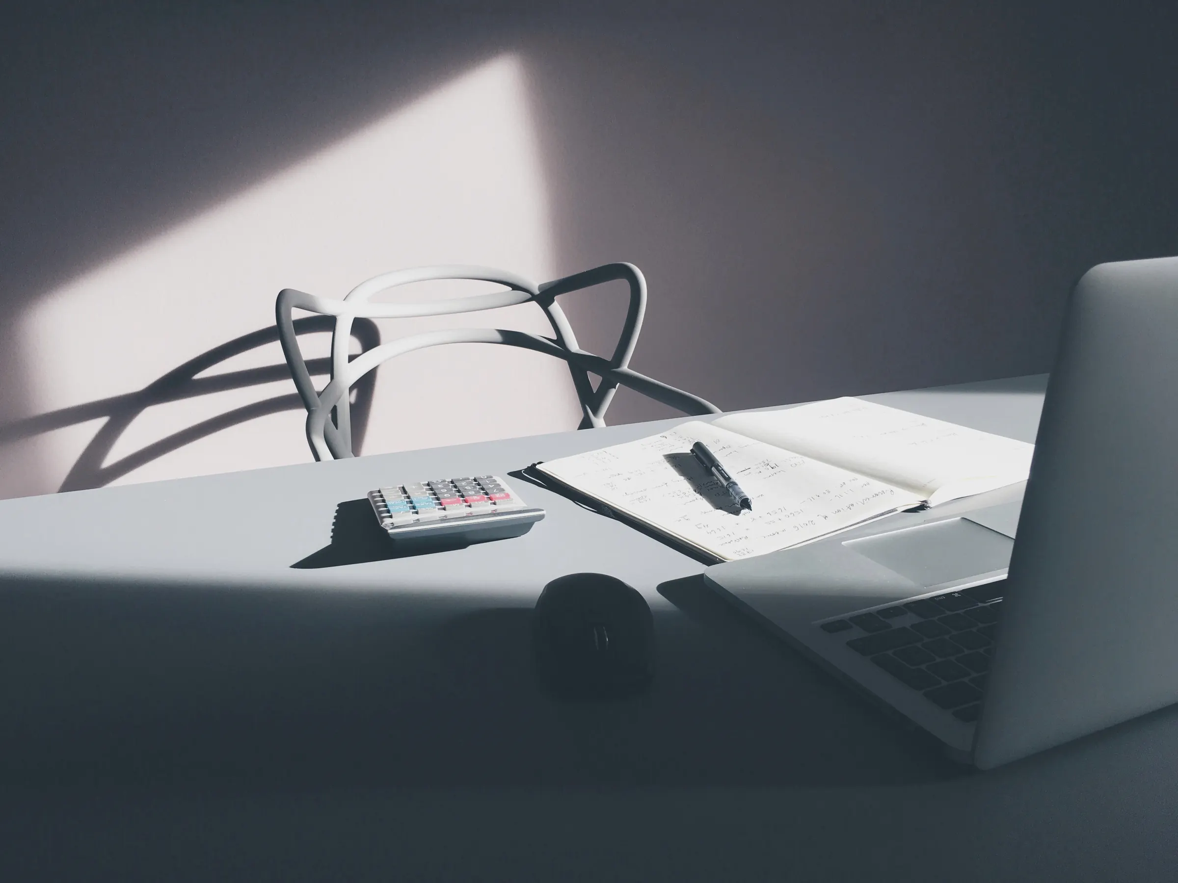A quiet desk with a laptop and notebook in soft window light.