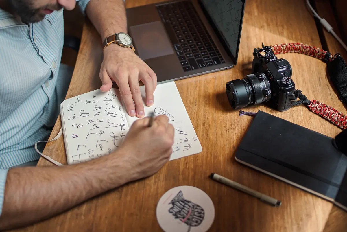 Hands sketching interface ideas in a notebook beside a laptop.