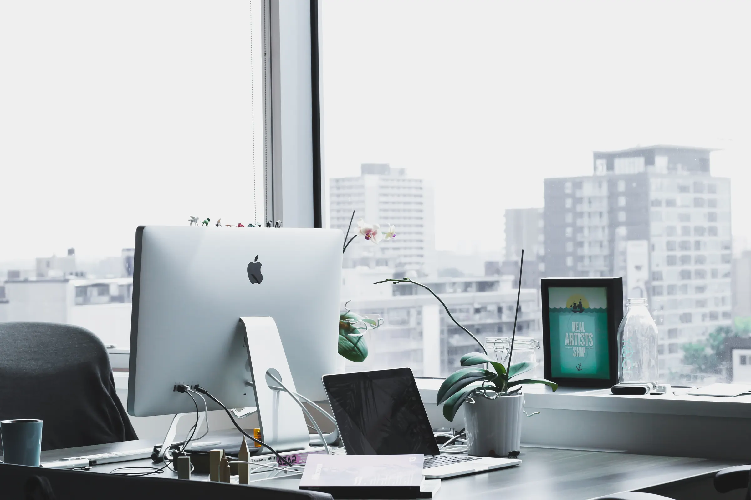 A tidy workstation with a large monitor beside a window overlooking the city.