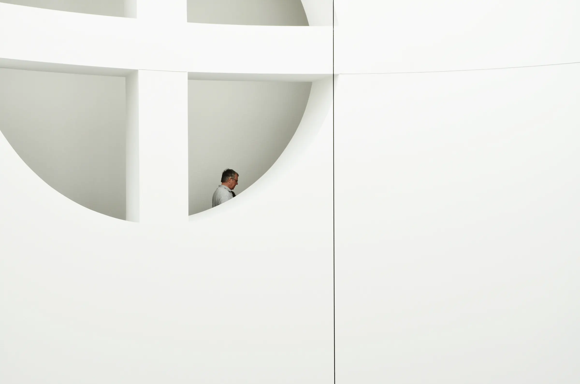 A person framed by a round opening in a white architectural wall.